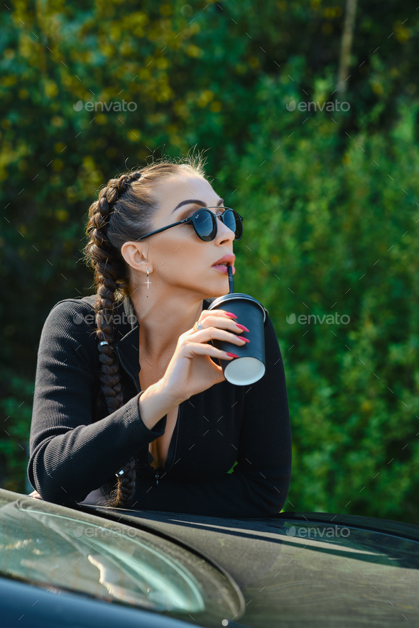 Woman leaning to the car and drinks strong coffee through the straw out of take away cup - Stock Photo - Images