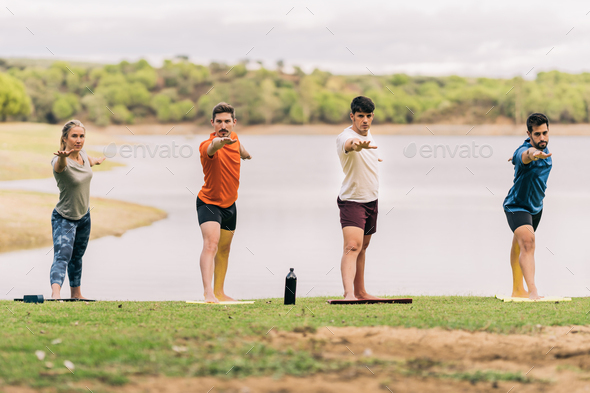 People in line raising arms while doing yoga in next to a lake