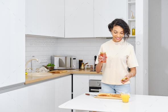 African american woman opens apricot jam to make sweet sandwich