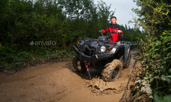Young man driving four-wheeler ATV through mud
