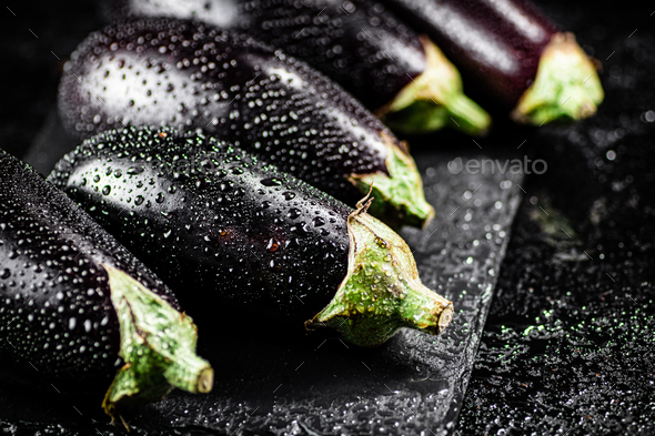 Fresh ripe eggplant with droplets of water on a stone board.