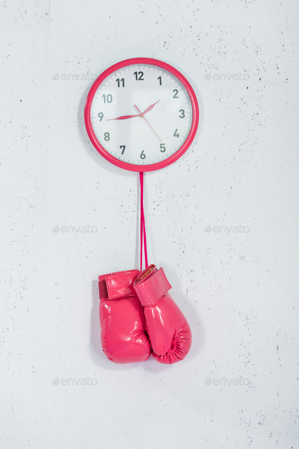 close-up view of pink boxing gloves hanging at wall clock on white