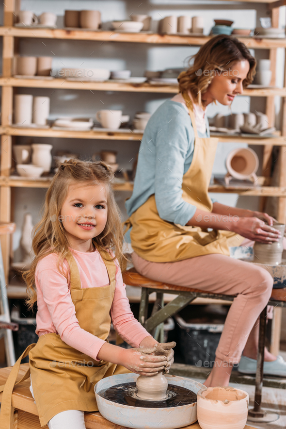 teacher and kid making ceramic pots on pottery wheels in workshop