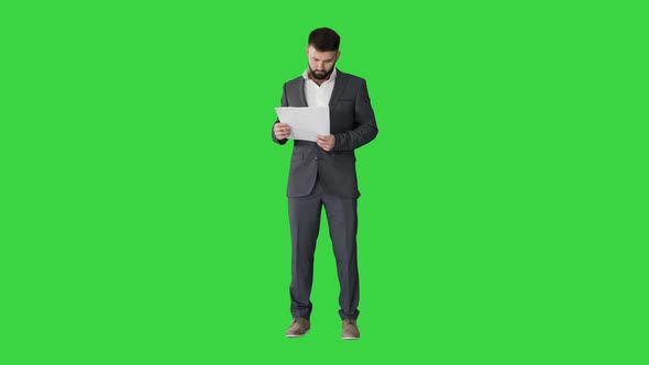 Businessman Standing and Reading Papers Seriously on a Green Screen, Chroma Key. alt