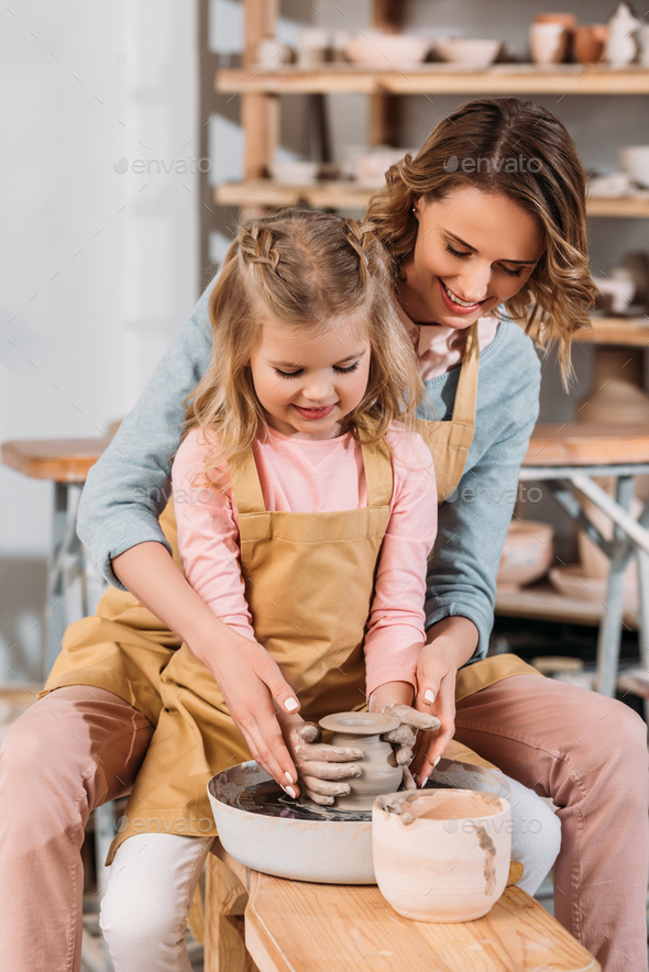 teacher and kid making ceramic pot together on pottery wheel