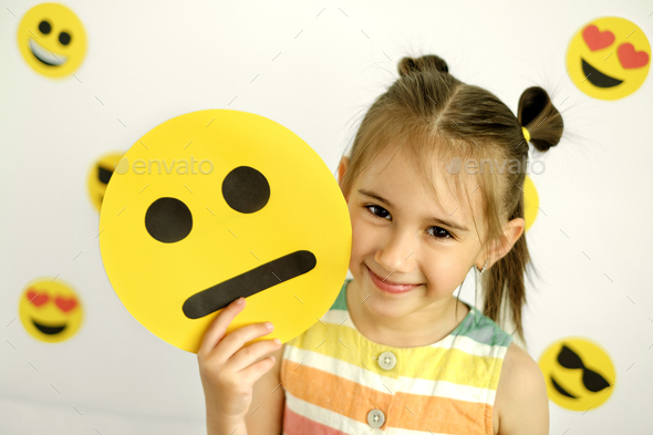 A cute beautiful smiling girl holds a cartoon cardboard sad face smile. - Stock Photo - Images