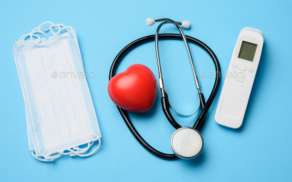 Non-contact thermometer, stethoscope and a stack of masks on a blue background
