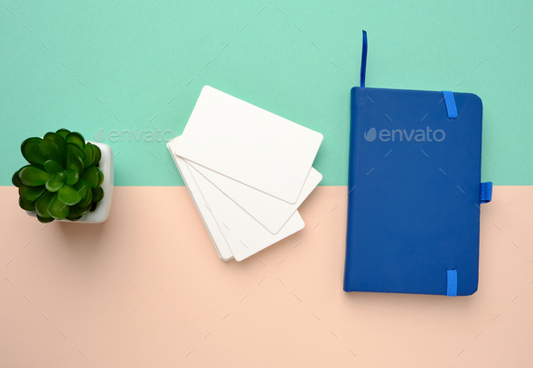 Stack of rectangular white blank business cards and blue notebook on a green beige background