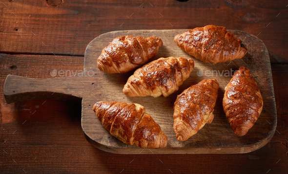 Baked croissants on a wooden brown board, delicious and appetizing pastries