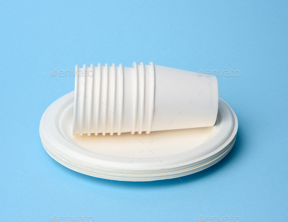 Stack of white paper cups and round plates on a blue background Stock ...