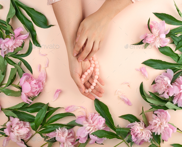 Two hands of a young girl with smooth skin and a bouquet of pink peonies on a peach background