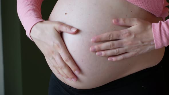 A pregnant woman stroking her bare pregnant belly.
