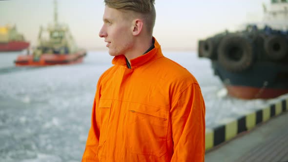 Dock Worker in Orange Uniform Looking at the Sea and Enjoying the Landscape of the Harbor in Winter alt