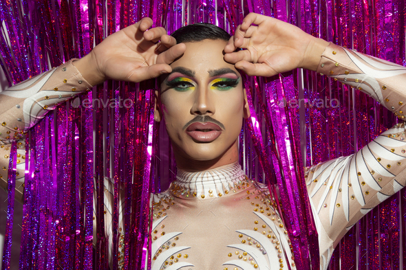 portrait of beautiful young man in drag queen makeup looking at camera and colorful background