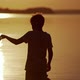 Backside view of a boy at sunset. Silhouette of the boy playing with origami boat on evening water - VideoHive Item for Sale
