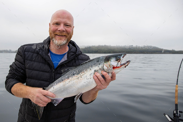 Happy fisherman holding fresh caught Coho salmon on Puget Sound
