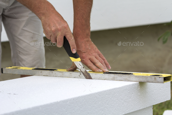Close-up of worker hand with knife and level cutting white rigid polyurethane foam