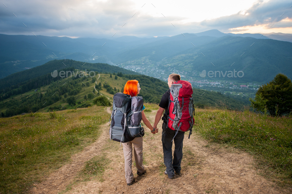 Back view of happy man and red-haired woman walking, holding hands ...