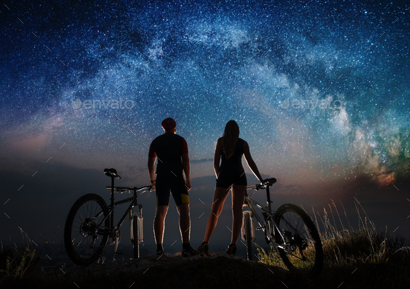 Couple cyclists with mountain bikes at night under starry sky