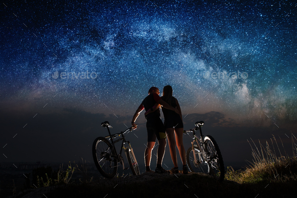 Couple cyclists with mountain bikes at night under starry sky
