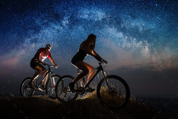 Sporty couple riding a bicycles at night under starry sky