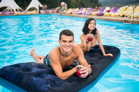 Happy brunette woman and the man having fun on a mattress at the swimming pool. - Stock Photo - Images