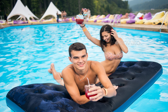 Happy brunette woman and the man having fun on a mattress at the swimming pool. - Stock Photo - Images