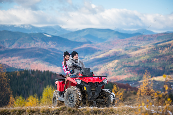 Happy couple on red four-wheeler ATV in mountains.