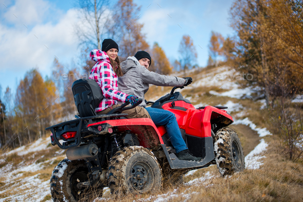 Happy couple on red four-wheeler ATV in mountains.