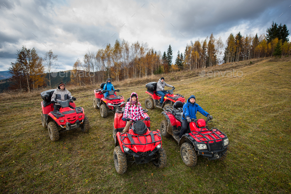 Young people in winter clothes on five red quad bikes on a countryside trail.