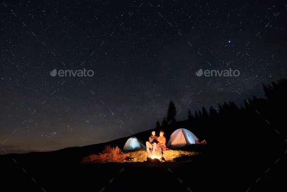 Tourists near campfire and tents under night starry sky