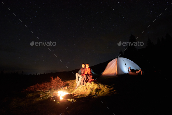 Tourists near campfire and tent under night starry sky