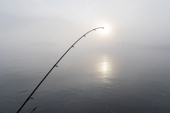 Fishing pole early morning on dark, foggy river Stock Photo by MatHayward