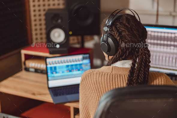 Musician with headphones sitting at desk with laptop while recording new song in the music studio - Stock Photo - Images