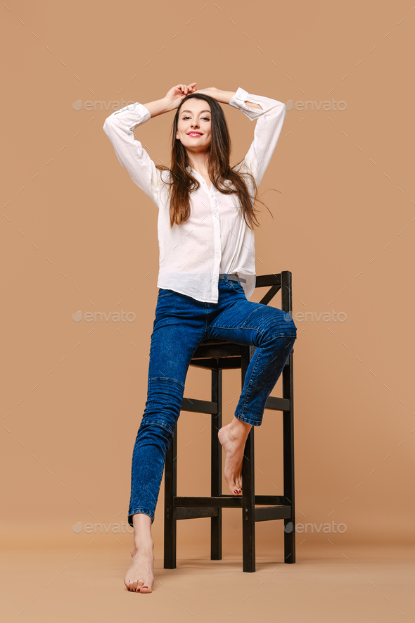 Girl with bare feet and in casual outfit posing at tall wooden