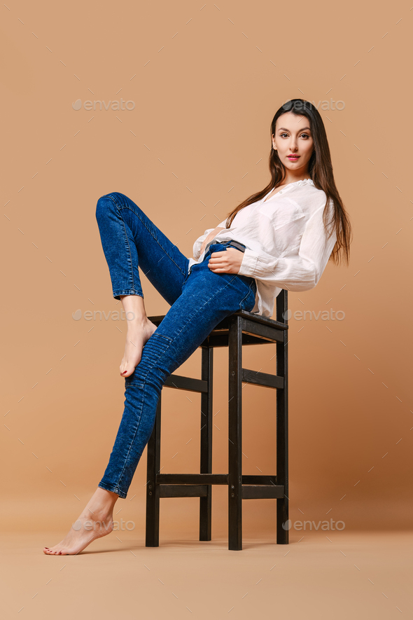 Girl with bare feet and in casual outfit posing at tall wooden stool