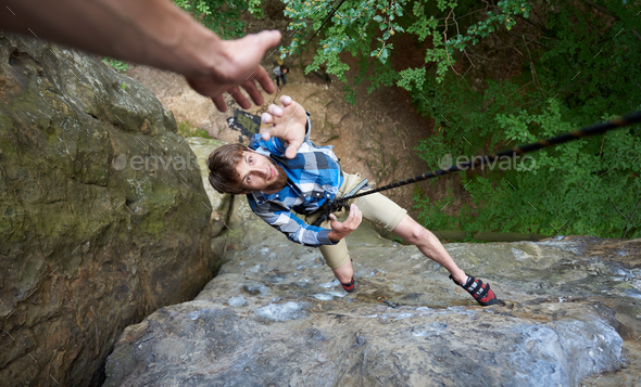 Climber hanging on rope between rocks and stretching out his hand. Hand helping in the rock climbing