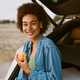 Young multiracial woman eating peach while sitting in trunk - PhotoDune Item for Sale