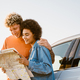 Multiracial couple smiling and examining map during car trip - PhotoDune Item for Sale