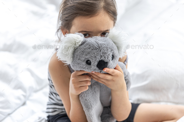 Happy little girl with soft toy koala in bed.