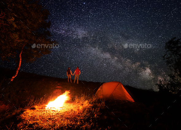 Night camping with a campfire under a bright starry sky with bright milky way