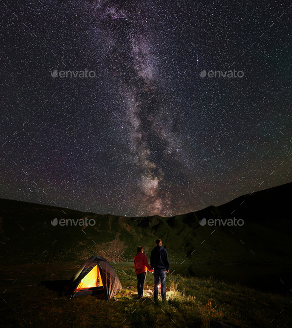 Back view couple holding hands enjoying starry sky and milky way by night campfire