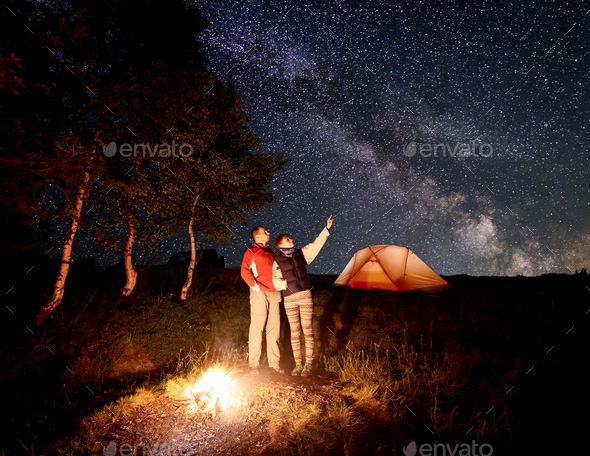 Woman shows the man up at the evening starry sky with Milky way