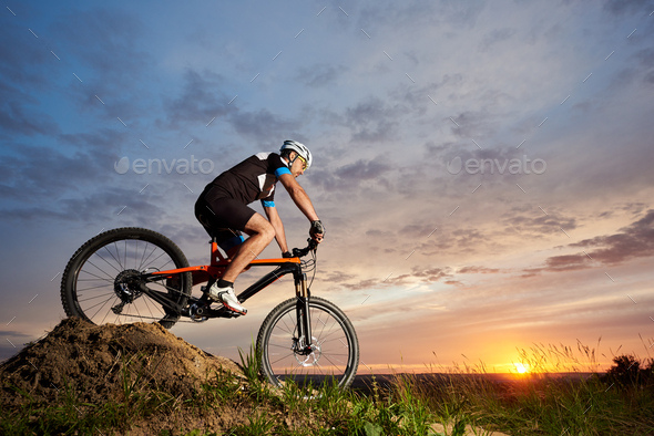 Athlete riding bike and rolling down hill against amazing sky background.