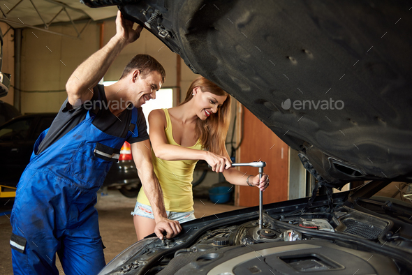 Young woman helps an auto mechanic repair car in garage