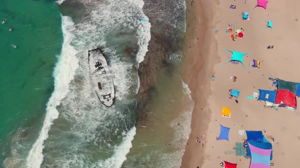 Picturesque summer beach with shipwreck and colourful umbrellas, aerial drone top down view 4k alt