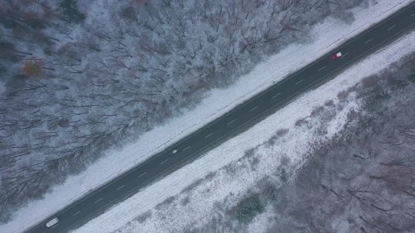 Aerial View of Traffic on the Road Passing Through the Winter Forest in Winter alt