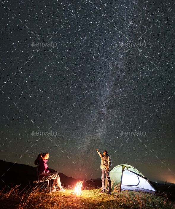 Couple tourists at night camp in mountains under starry sky