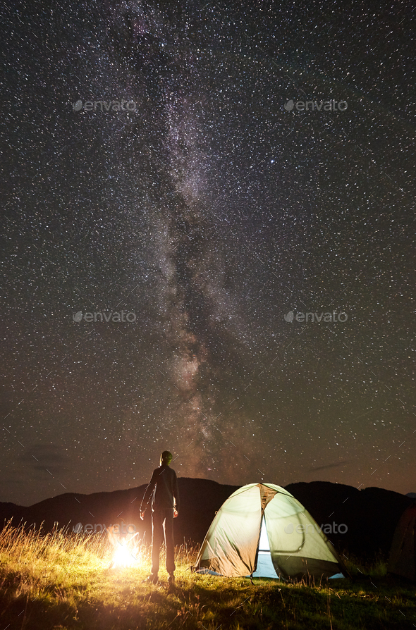 Man resting at camp and tent under under night starry sky