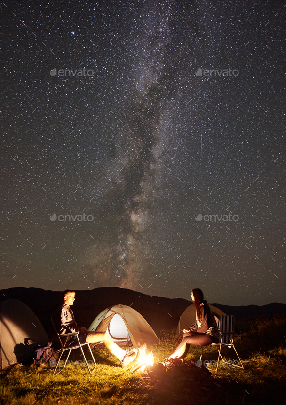 Couple tourists at night camp in mountains under starry sky